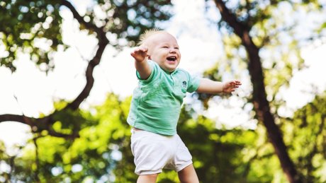 Lite barn blir løftet opp i luften utendørs, med grønne trær i bakgrunnen.