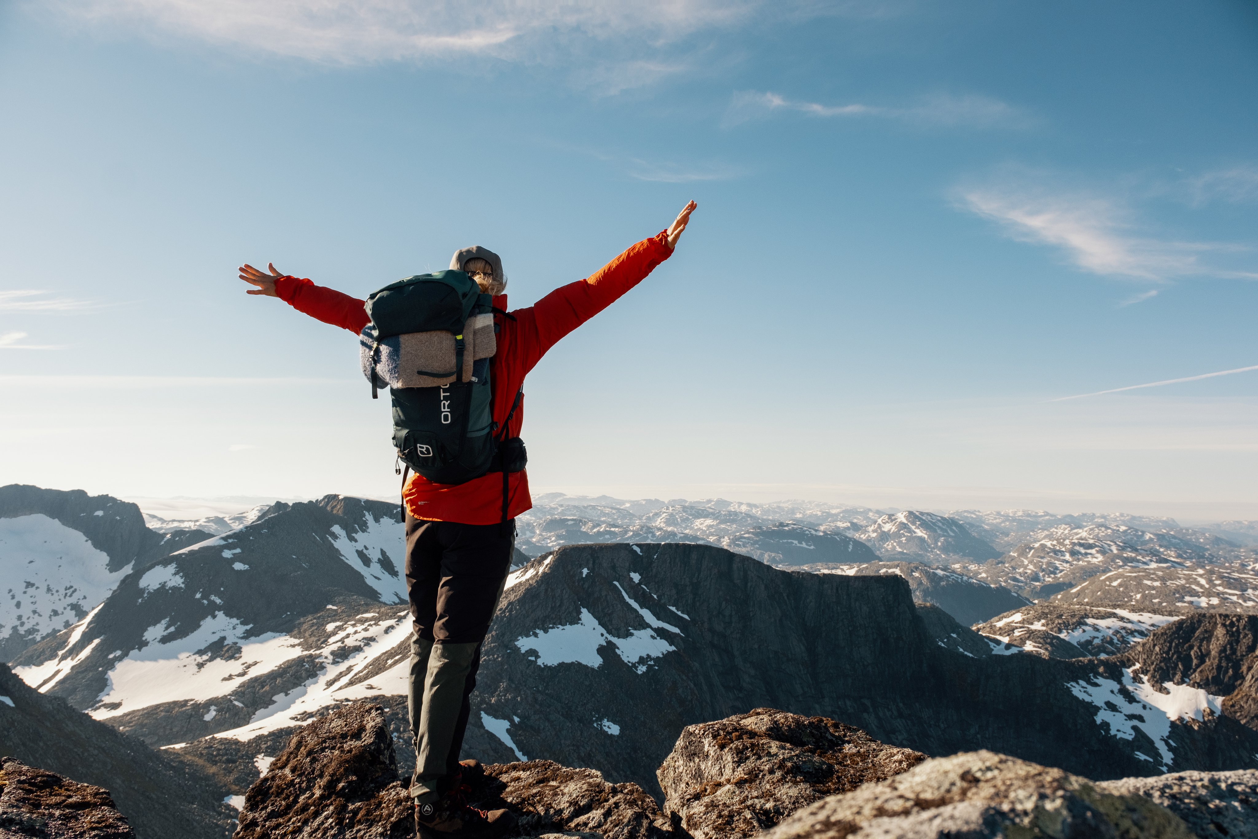 En kvinne står på toppen av et fjell og ser utover landskapet.