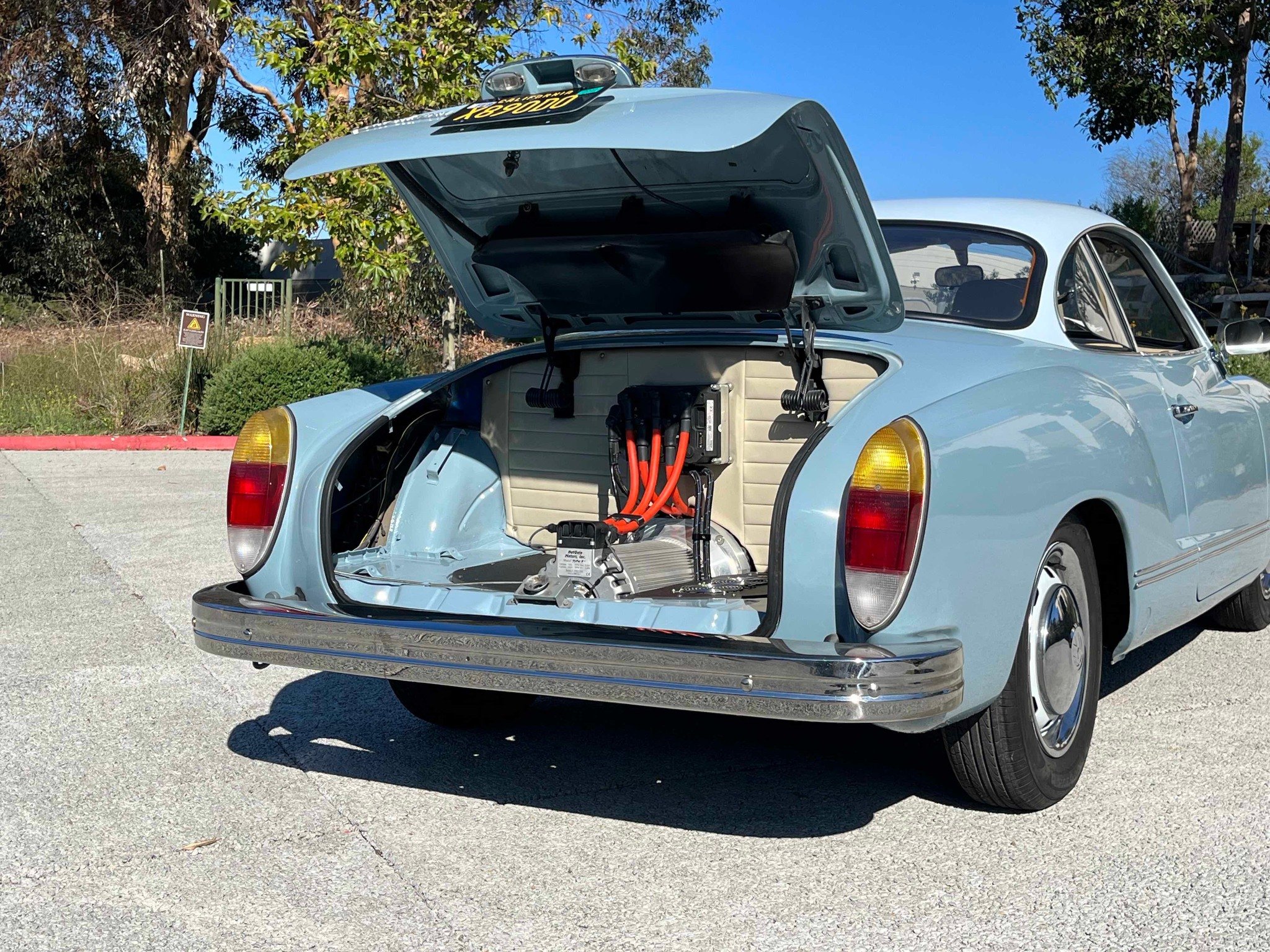 Gammel bil med åpen bakluke som viser elektrisk motor og høyspentkabler.