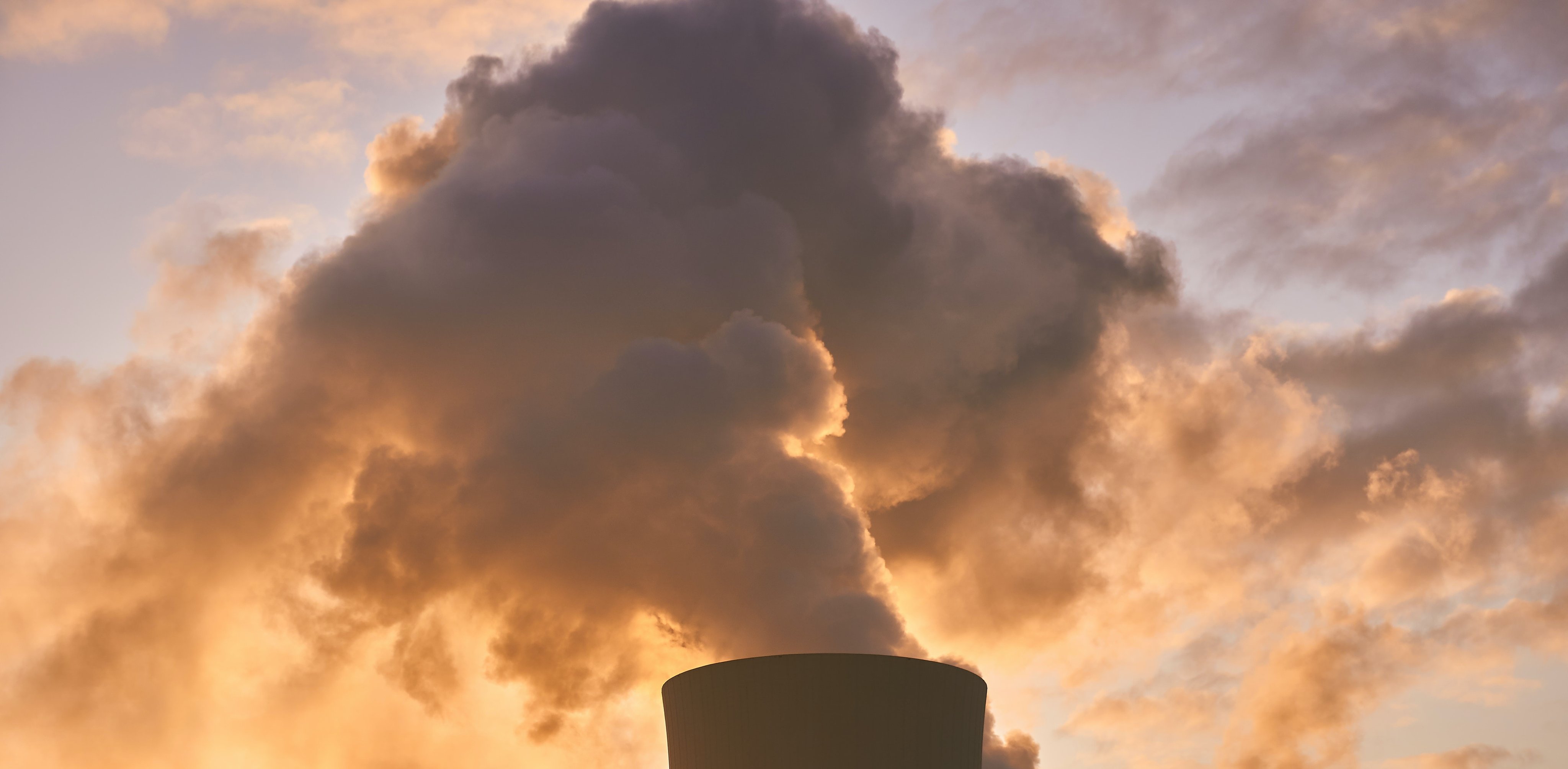 Gass eller røyk stiger opp mot en himmel med solnedgangsfarger.