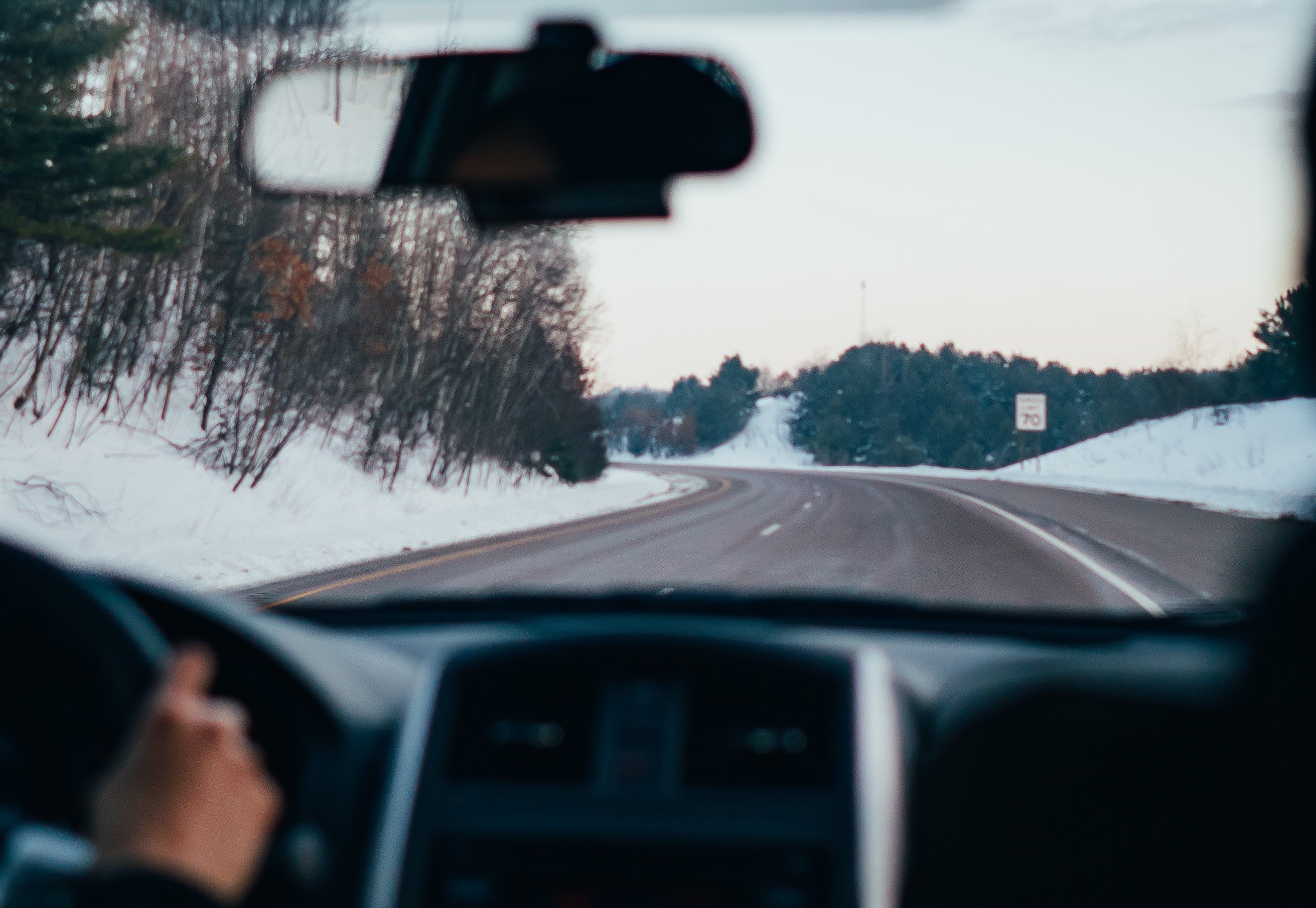 Det er snø langs bilveien og via frontruten inne i en bil, kan man se hovedveien bilen kjører på.