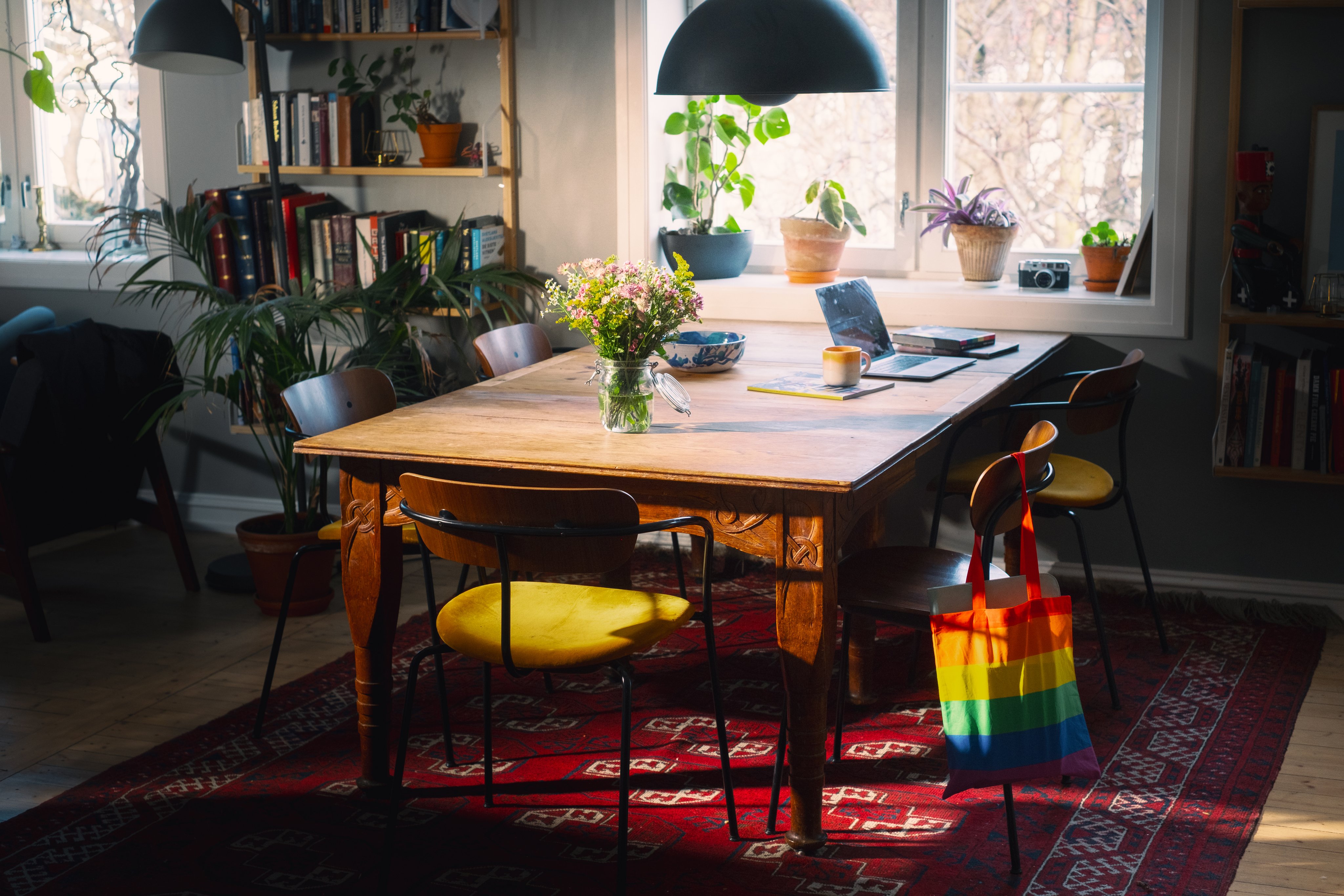 Lyst og hjemmekoselig kjøkkenbord omgitt av planter, bøker og varme solstråler.