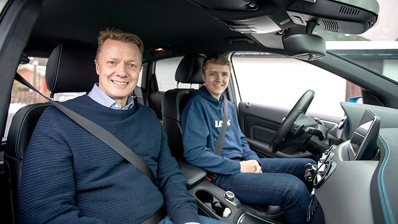 Svein Tore Stenvold og sønnen Fredrik inne i en bil, der sønnen sitter i førersetet og far i passasjersetet. Begge smiler til kamera