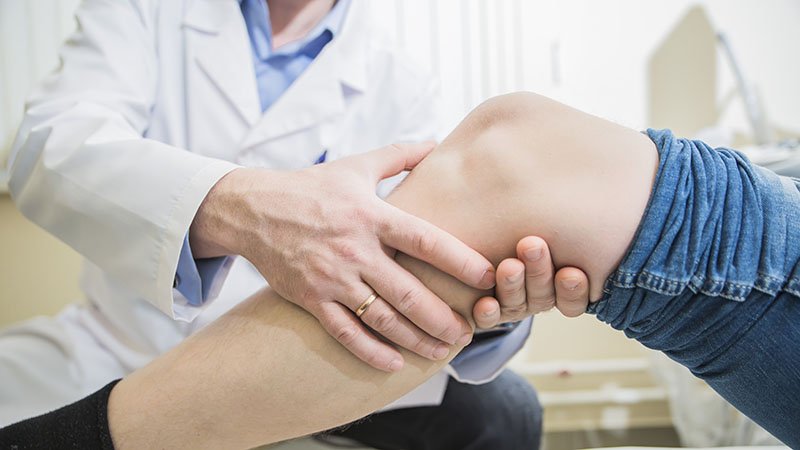 Lege undersøker et kne ved å holde og bøye benet.