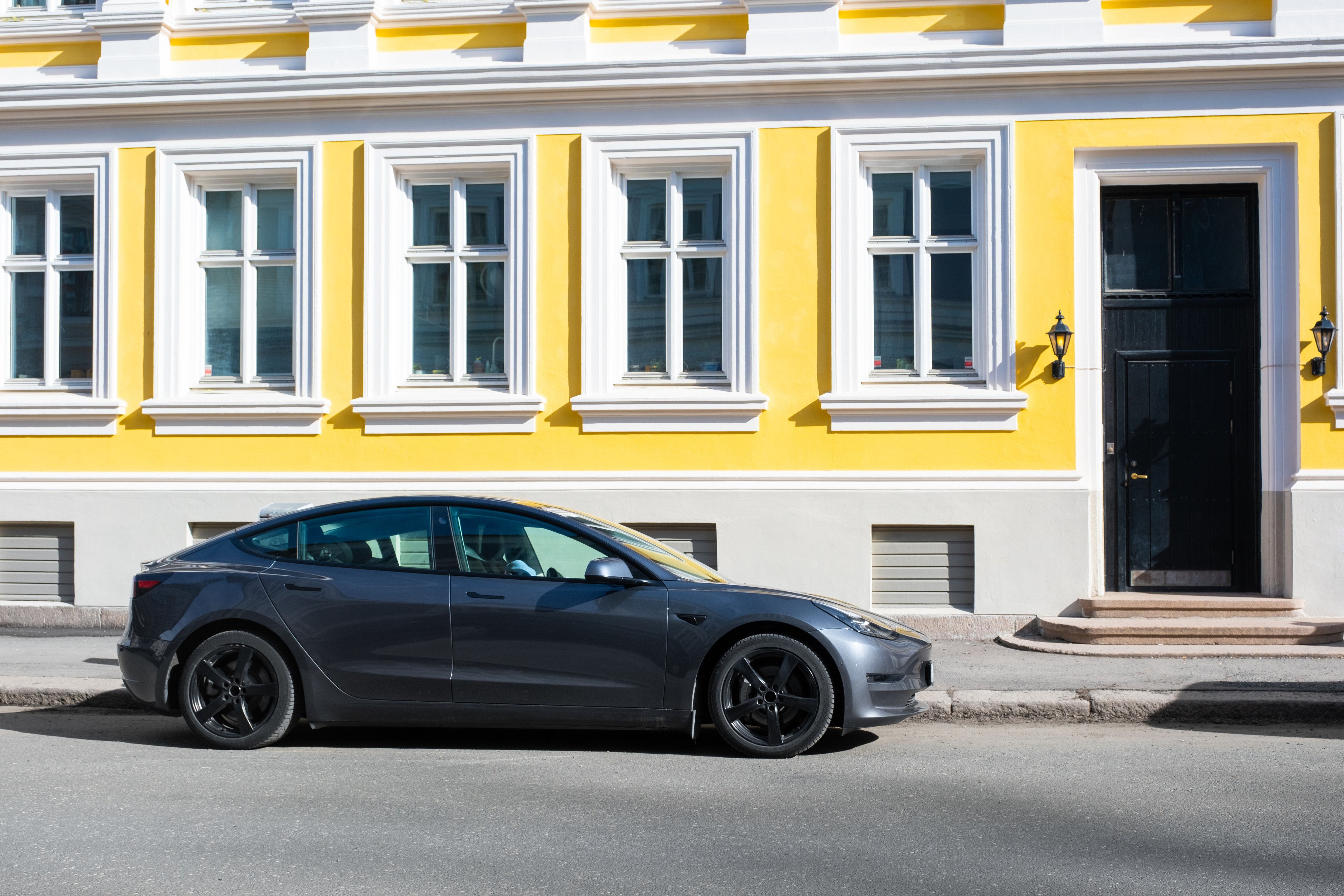 En elbil står parkert på gata i en by, foran en bygning i klassisk stil med mange leiligheter.