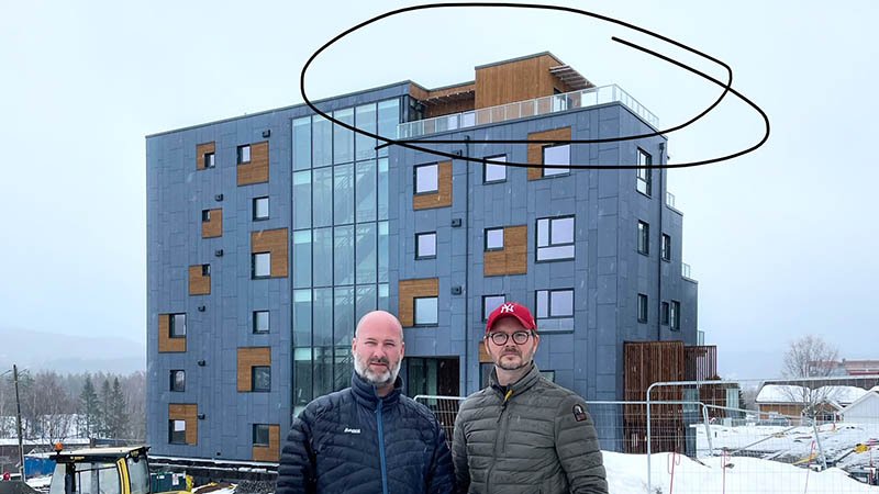 To menn står foran et stort og nytt boligkompleks. Det er vinter og overskyet.