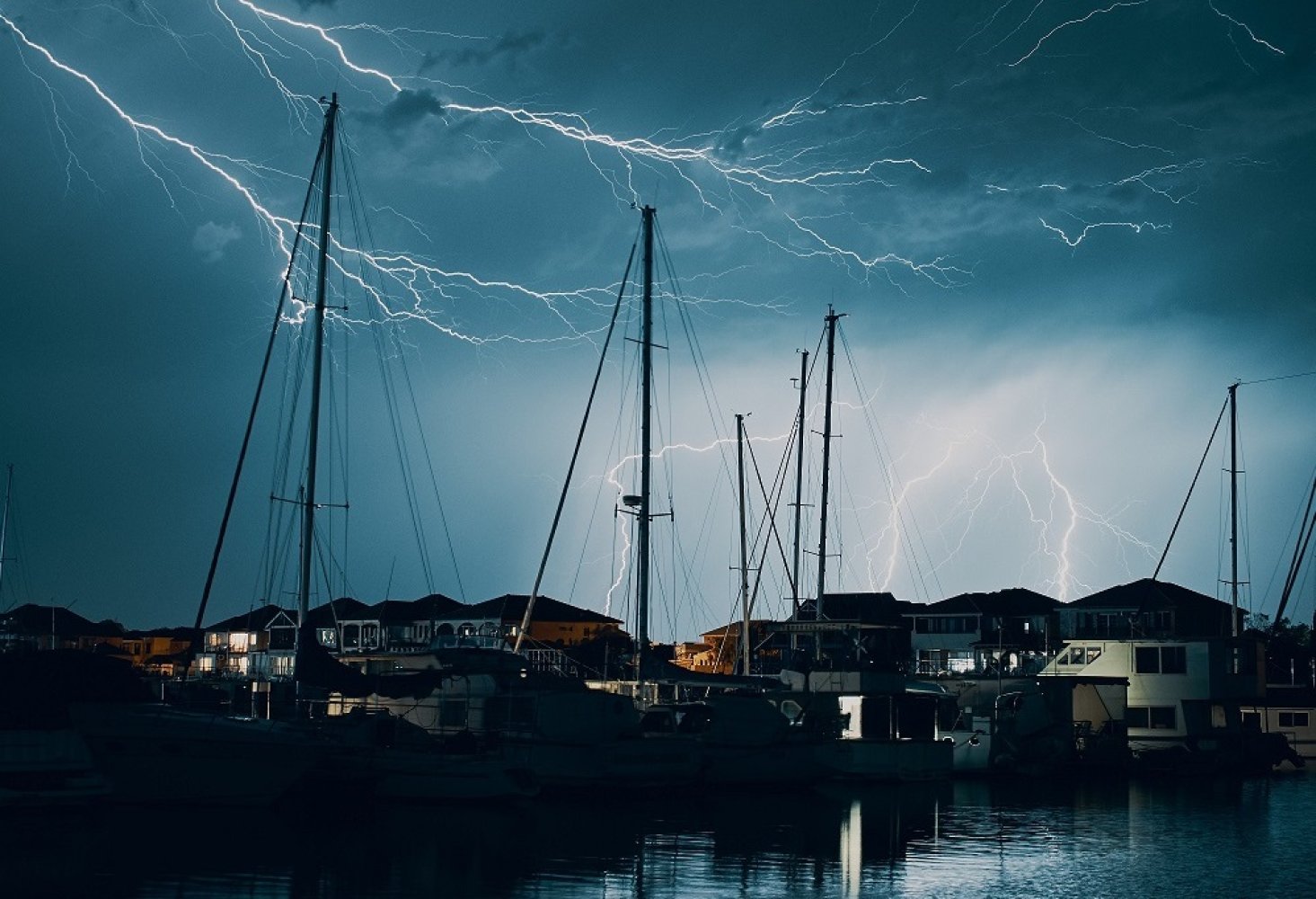Det er natt og lyn på himmelen over en havn med seilbåter.