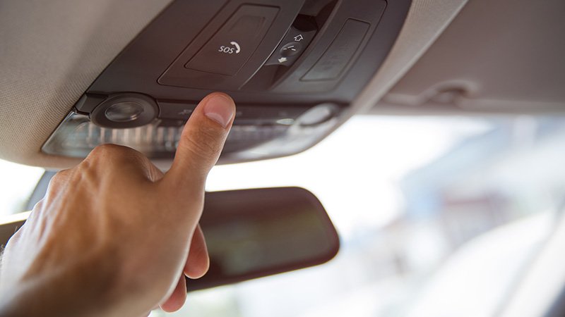 Hånd trykker på SOS-knapp i bilens takpanel nær bakspeilet.