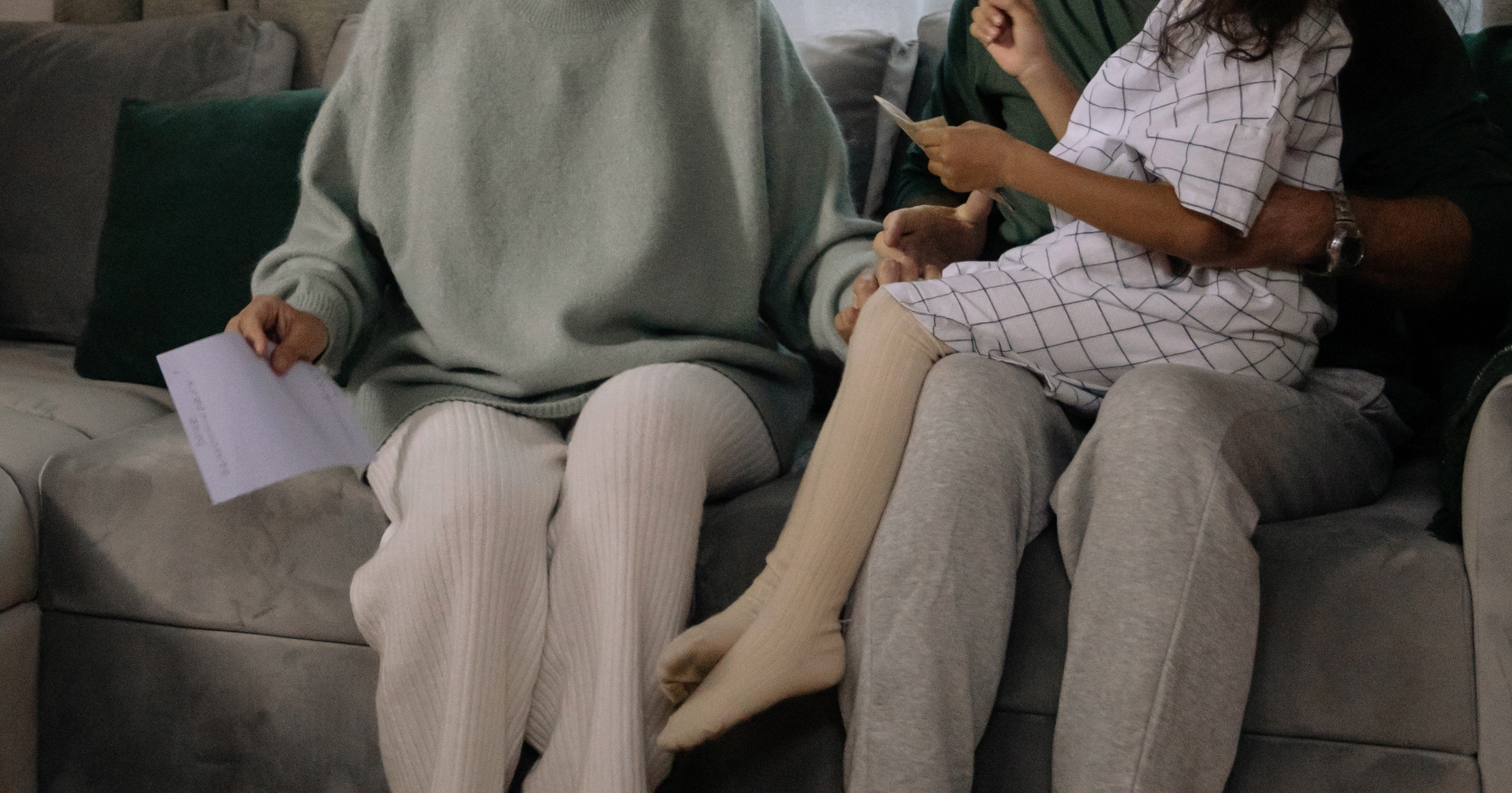 Tre personer sitter på en sofa; en voksen holder et barn på fanget mens en annen voksen holder et ark.