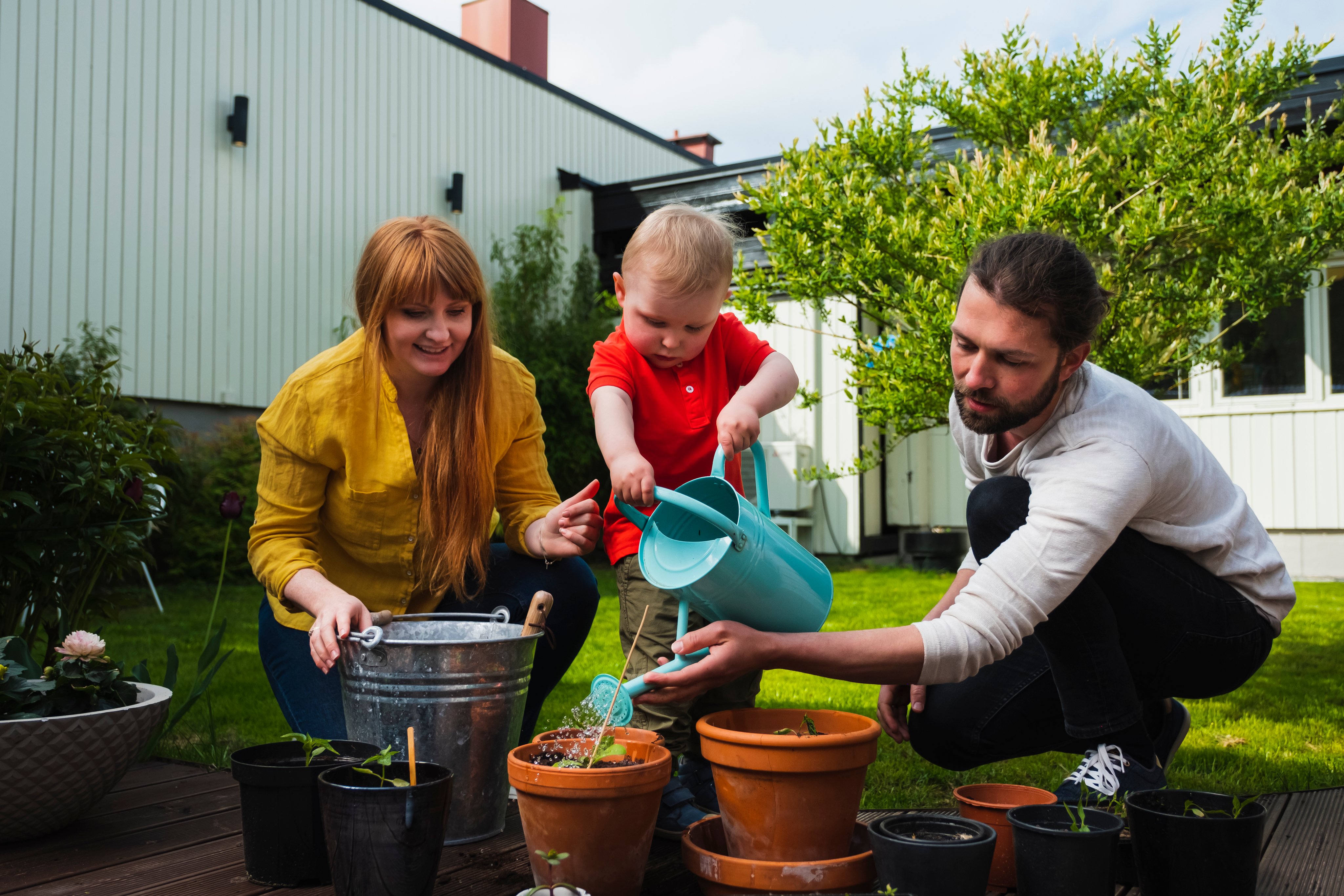 Voksne og barn planter og vanner små planter i potter på en terrasse i en hage.
