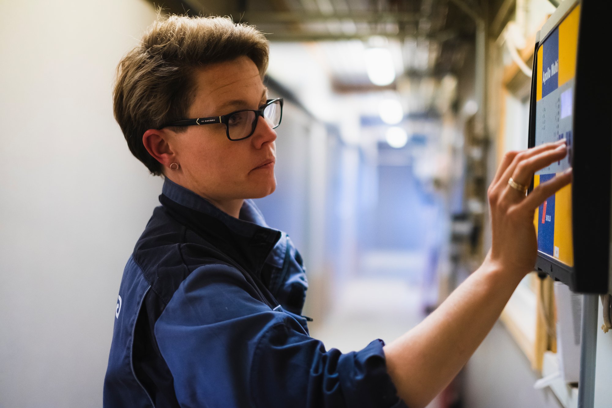 Kvinne som står og trykker på en skjerm på veggen inne i en bygning.