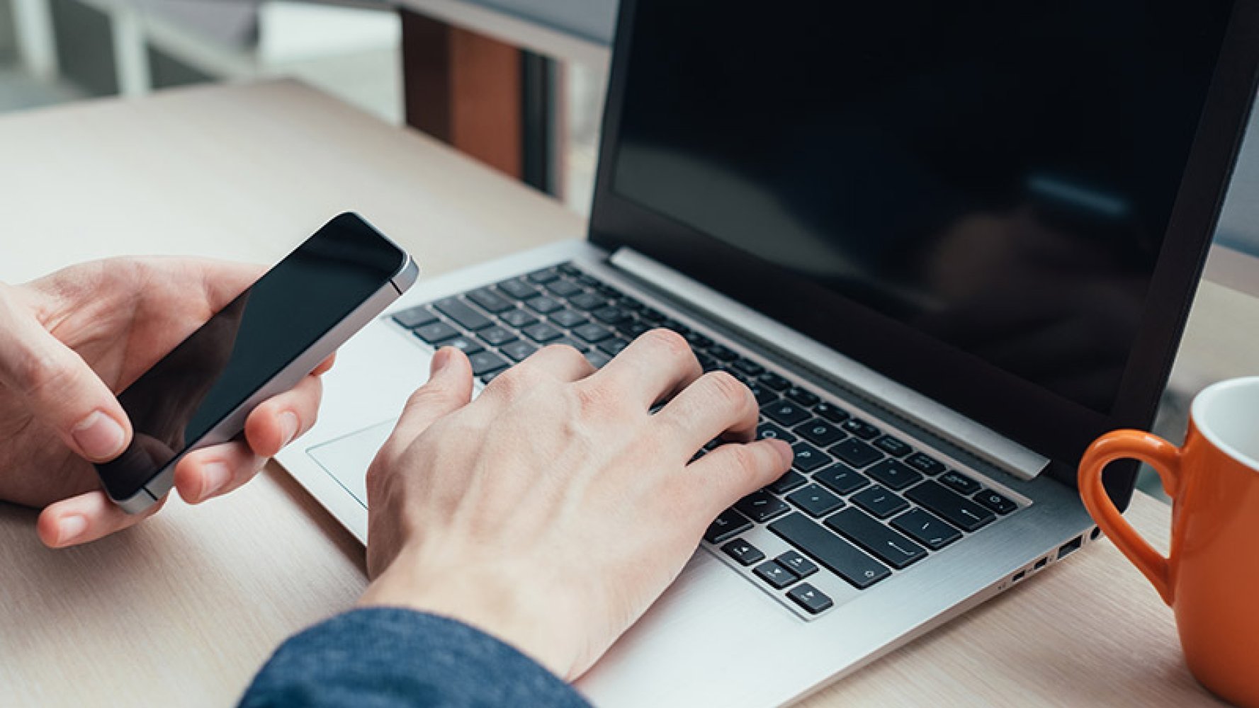 Person bruker bærbar PC og holder en smarttelefon.