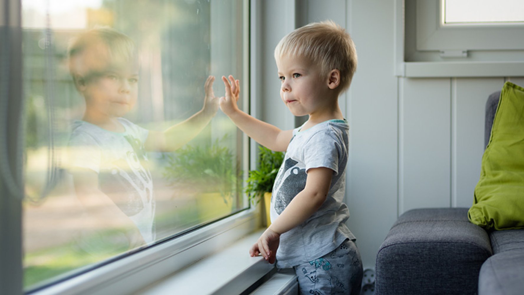 Barn i barnehagealder står ved siden av et vindu og ser ut.