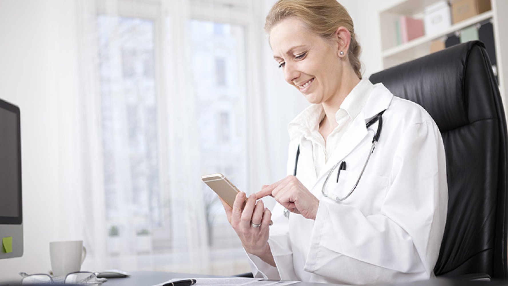 Lege sitter og trykker på mobilen sin på kontoret mens hun smiler
