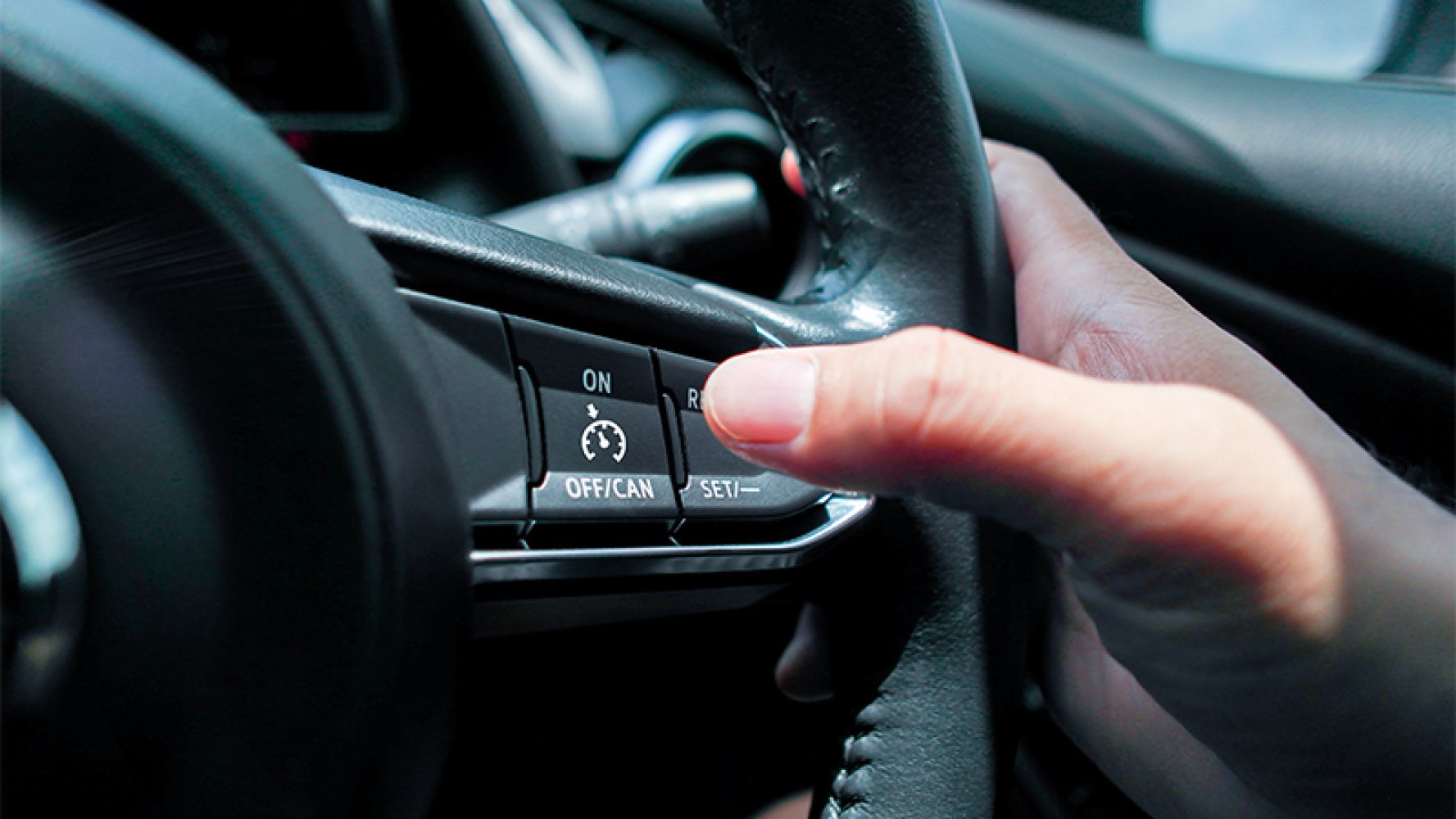 Nørbilde av en finger som skal trykke på cruisekontroll-knappen på et bilratt.