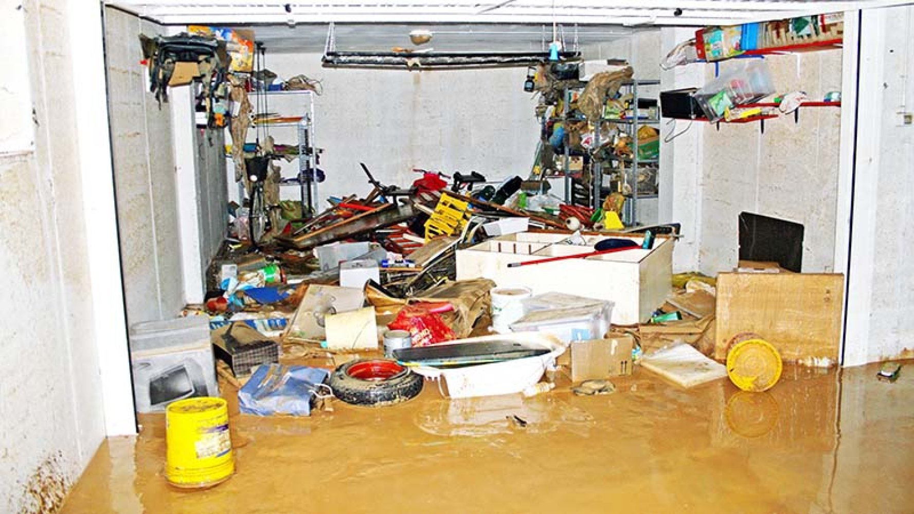 Kjeller fylt med vann og rot etter flom, med møbler og gjenstander spredt rundt.