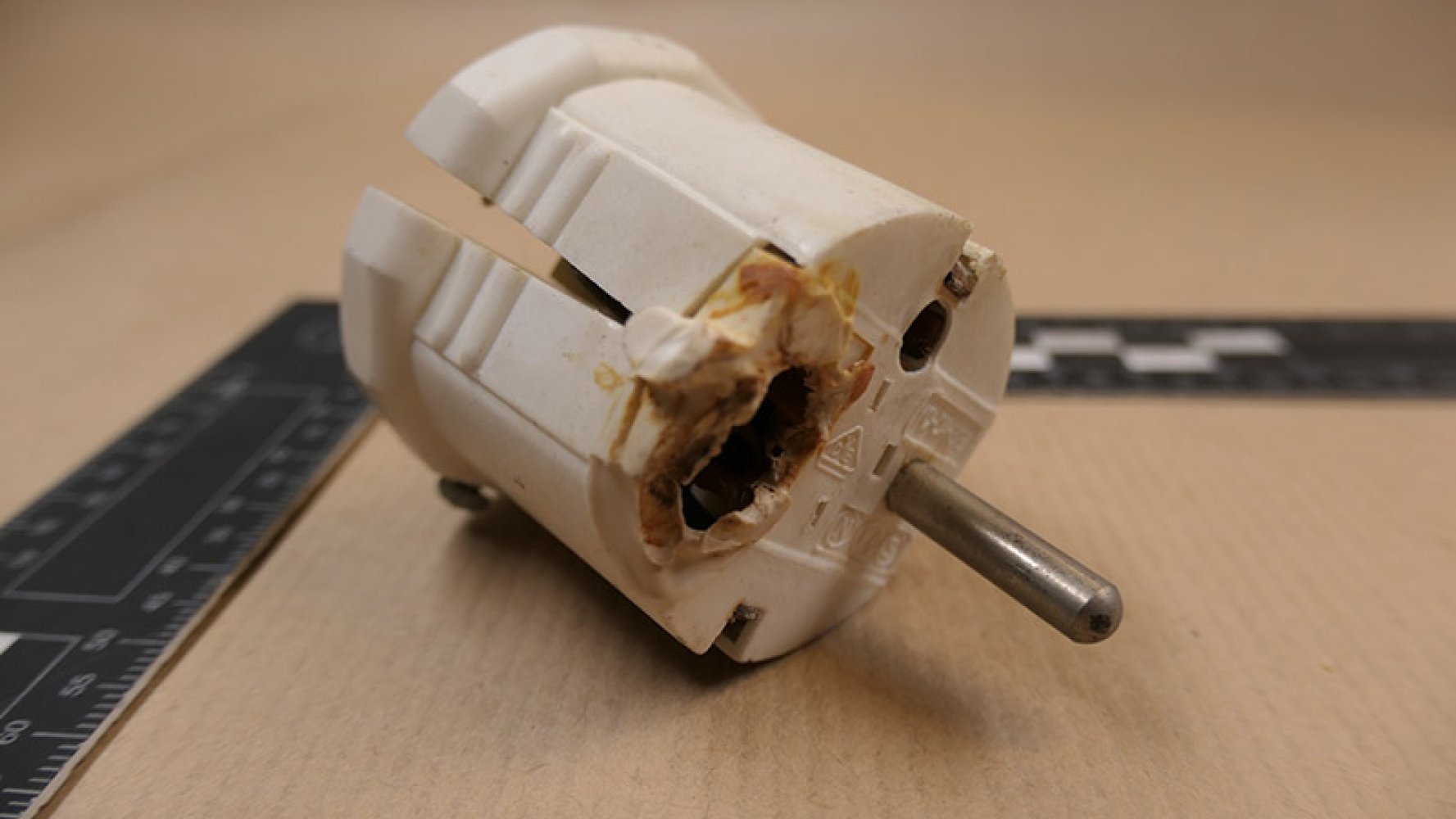 Nærbilde av en brent og skadet støpsel med misfarging rundt kontakthullene.