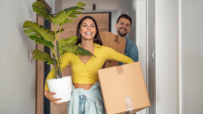 Et ungt par bærer esker og planter inn i en leilighet.