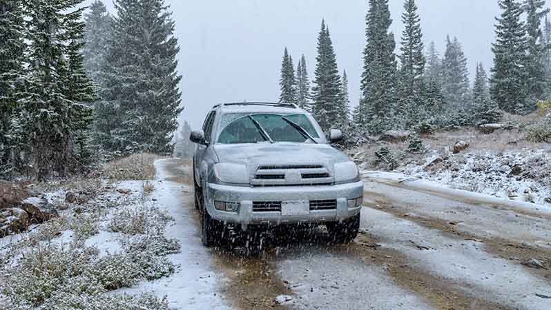 Solfarget bil parkert på en sandvei til fjells med lett snøfall rundt