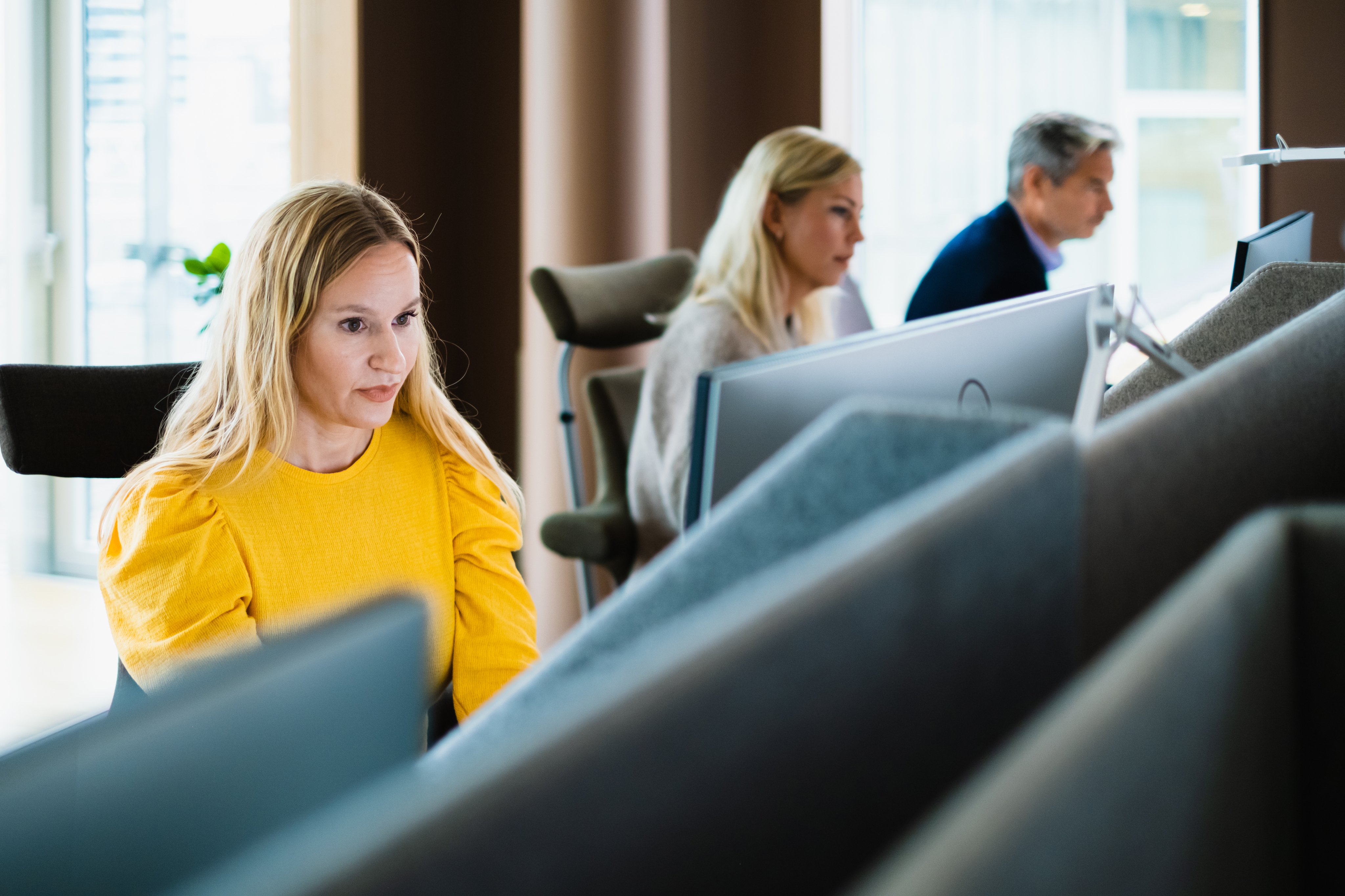 Flere ansatte sitter og jobber ved dataskjermer i et moderne kontorlandskap.