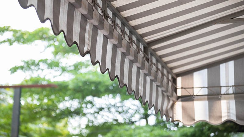 Stripete markise over uteområde med grønne trær i bakgrunnen.
