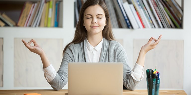 En jente sitter foran pc-en med armene oppgitt ut til siden.