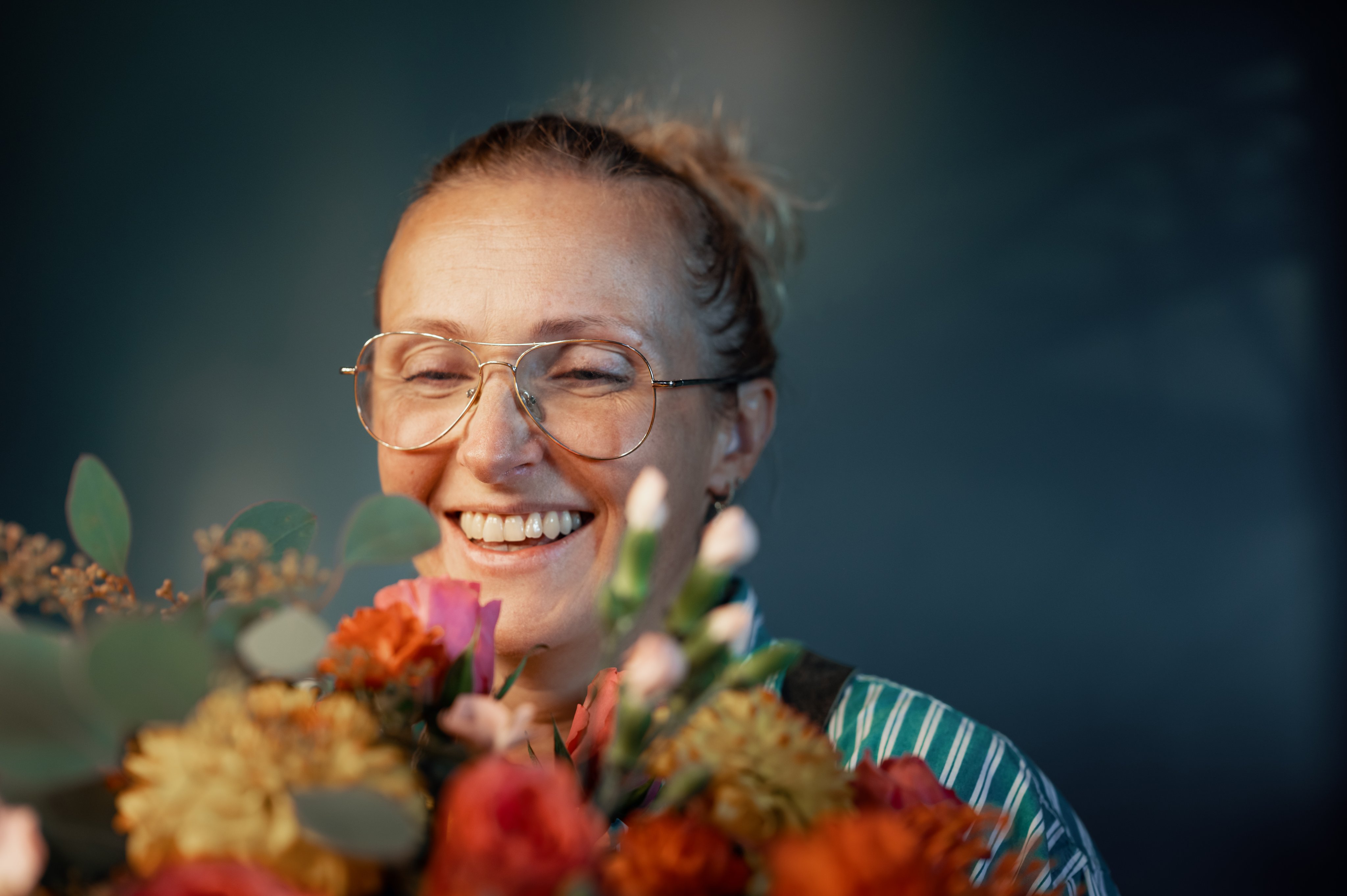 En ansatt på blomsterbutikk som smiler mens hun holder i en bukett.