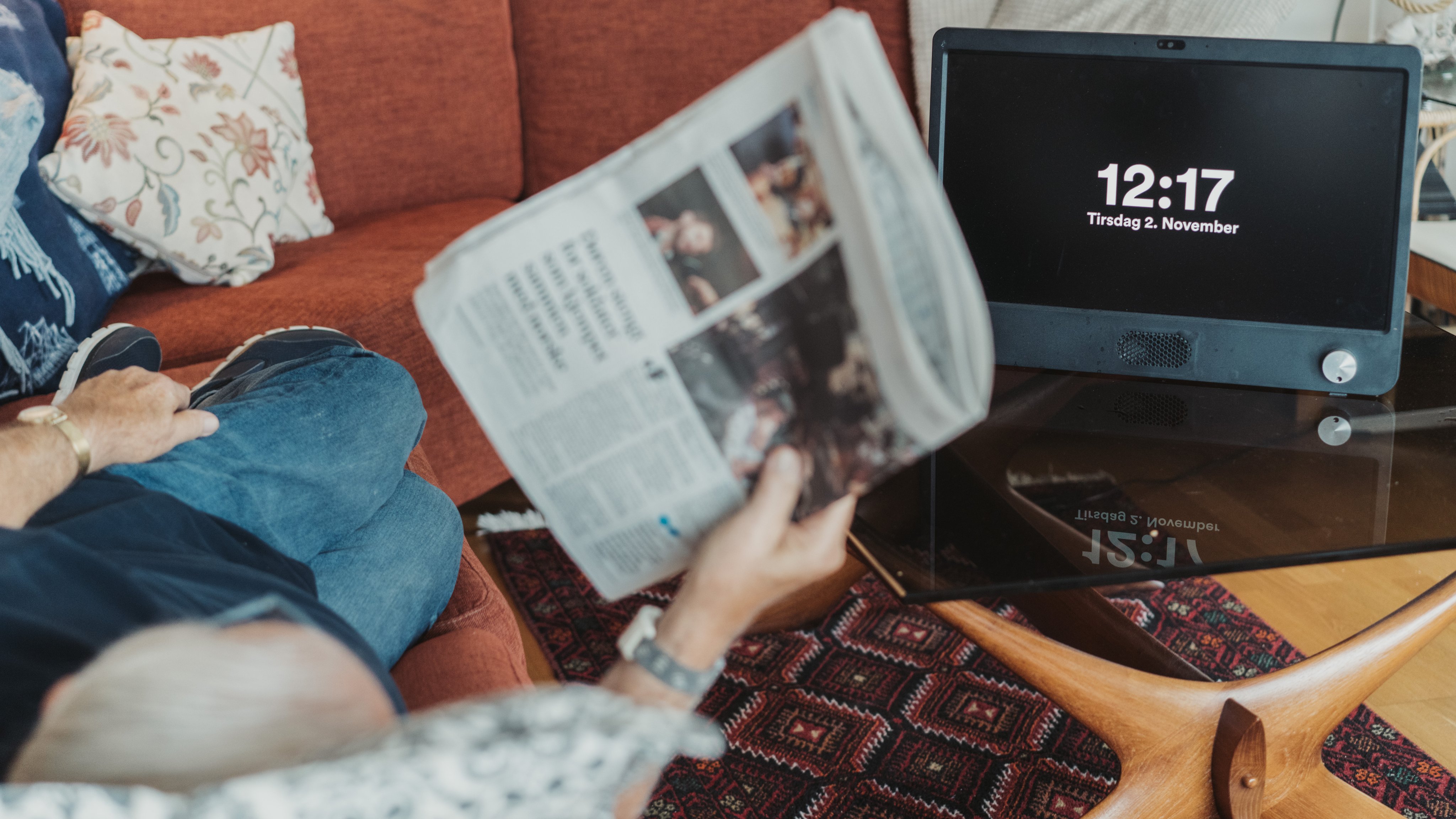 En mann ligger på sofaen og leser avisen