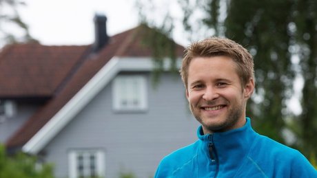 Simon står foran et hus og smiler til kameraet.