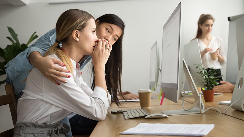 En kollega trøster en annen ved en kontorpult i et åpent kontorlandskap.