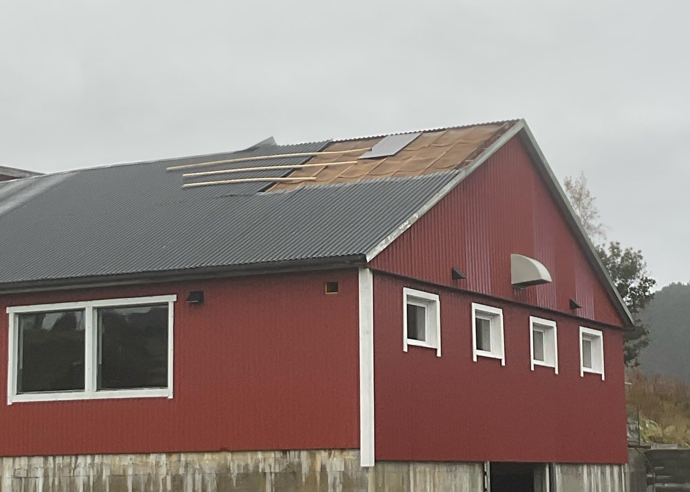 Rød låve med ødelagt tak. Grå himmel og skyer.