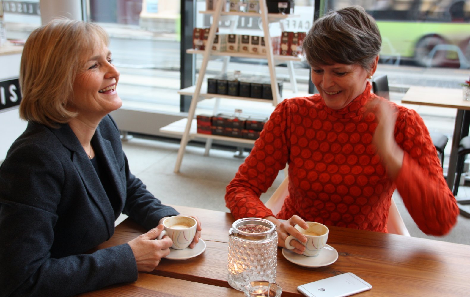 To godt voksne kvinner sitter på cafe og hygger seg sammen.
