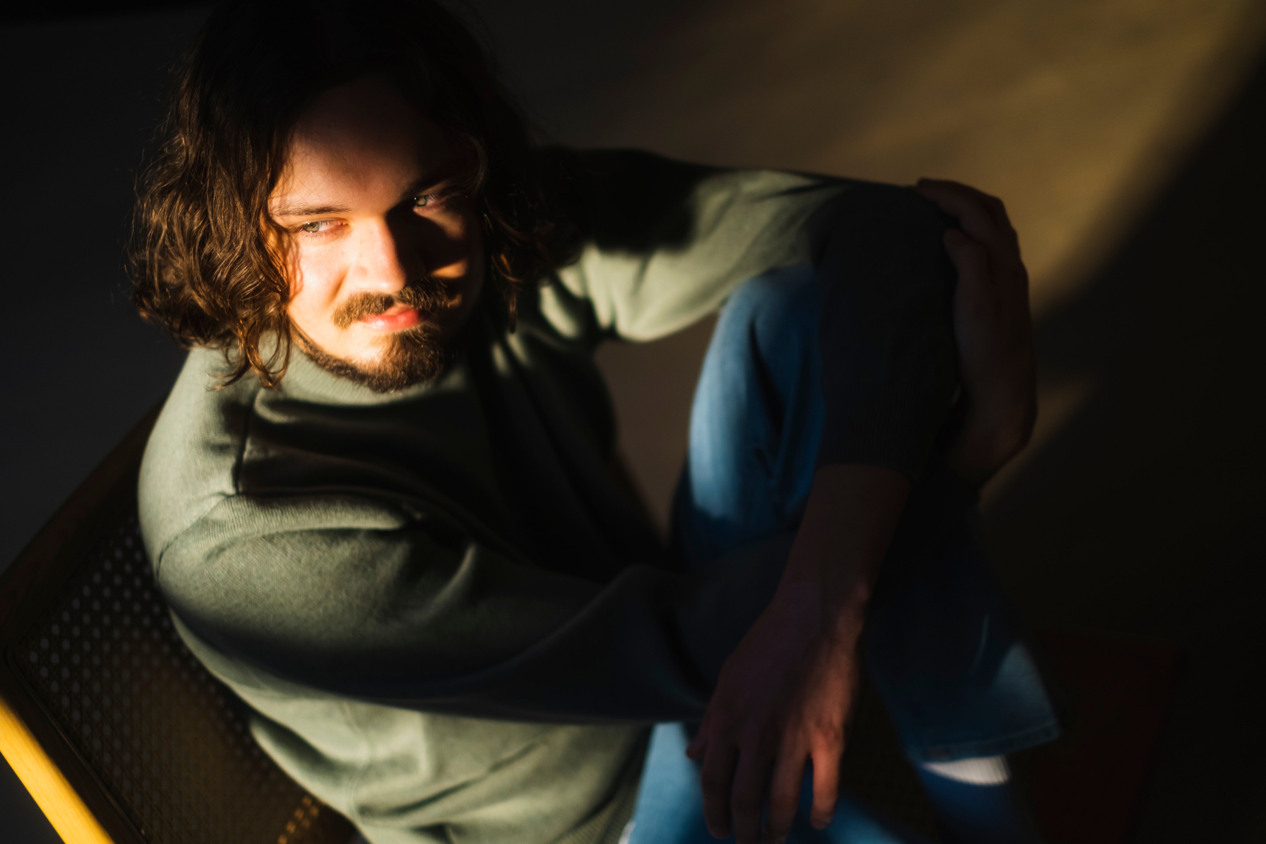 Naturlig sollys treffer mann som sitter på gulvet i et mørkt rom, viser kontrast mellom lys og skygge.