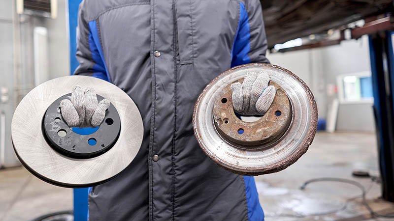 En person som holder to bremseskiver. Den ene er rusten og slitt.