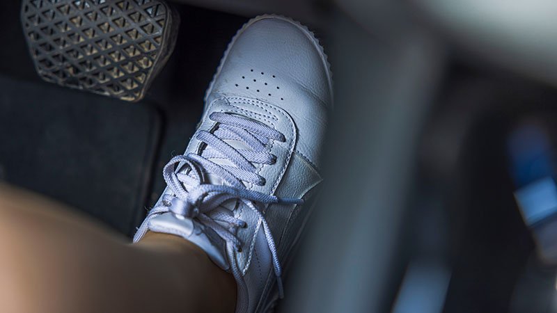 Nærbilde av en fot med hvit sko som trykker ned gasspedalen på en bil.