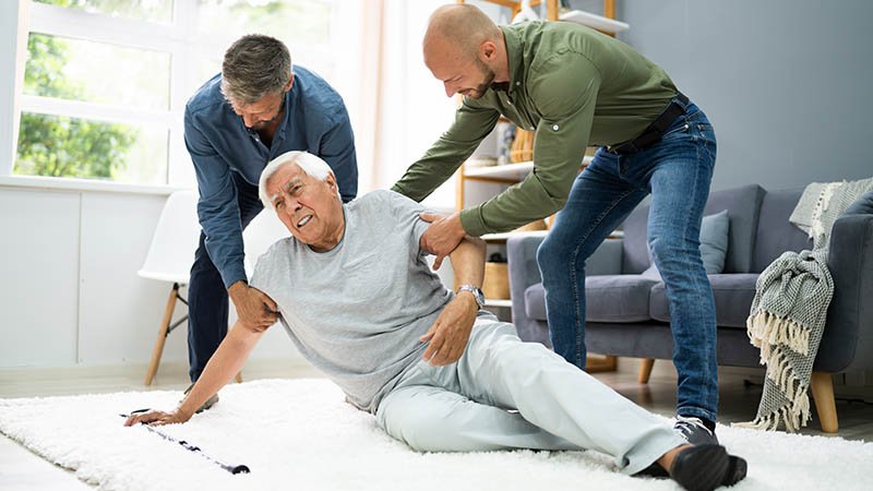 To menn hjelper opp en eldre mann som ligger på bakken.