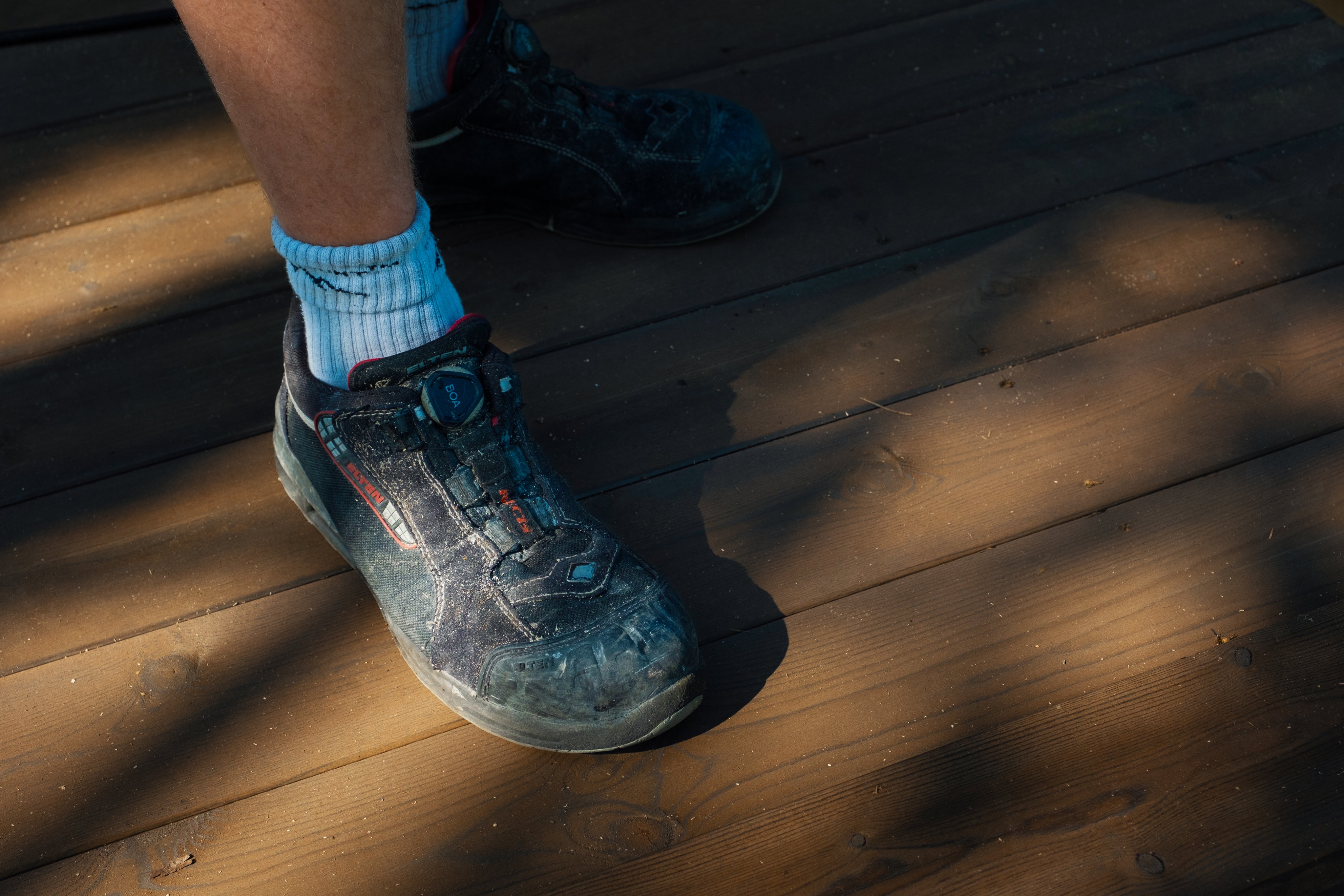 Sko og sokker på en person som står på trestokk eller treplanke.