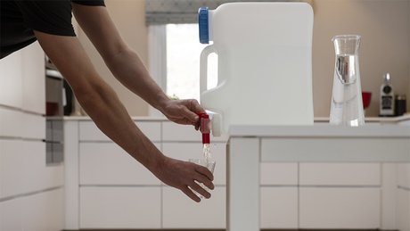 En mann tapper vann fra en vanndunk på kjøkkenet.