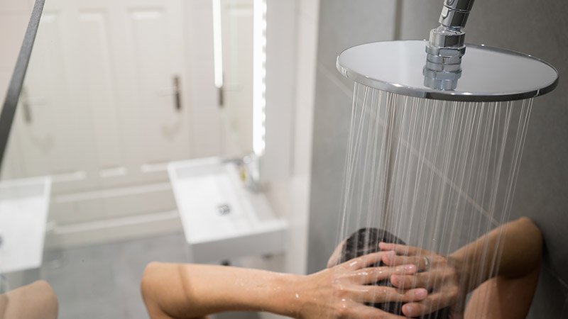 Person som står i dusjen under en rund dusjhode med rennende vann.
