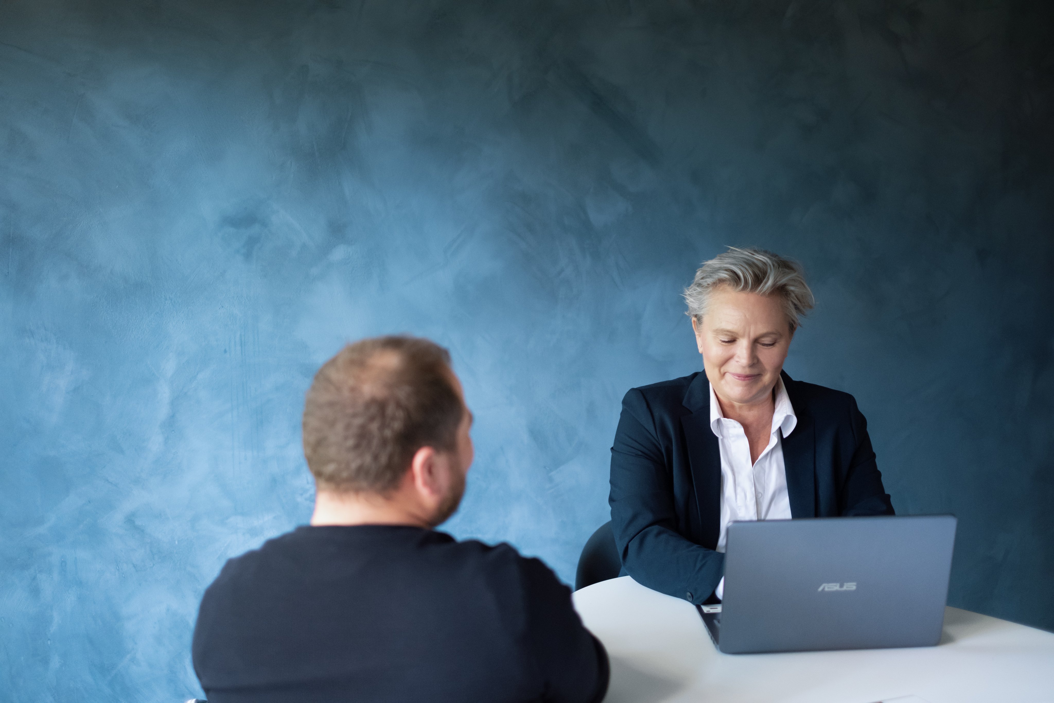 To personer sitter ved et bord, den ene har pc foran seg