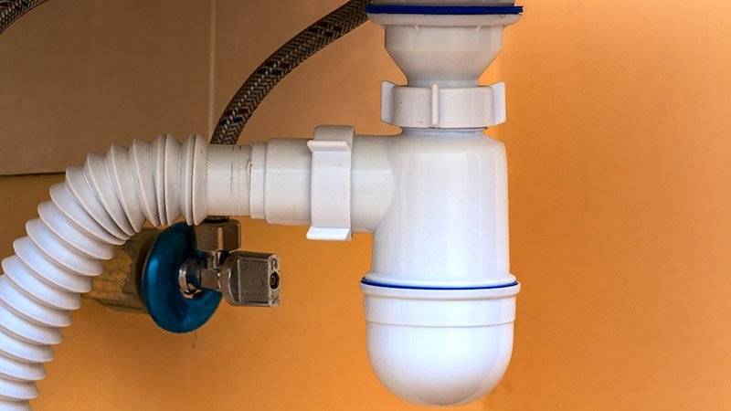 Hvitt avløpsrør med slange og ventil under en vask.