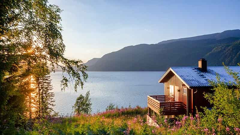 Idyllisk, rød hytte ved stort vann eller fjord ved solnedgang. 