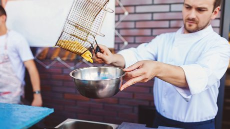 Mann i kokkeuniform holder en frityrkurv med pommes frites over en bolle på kjøkkenet.