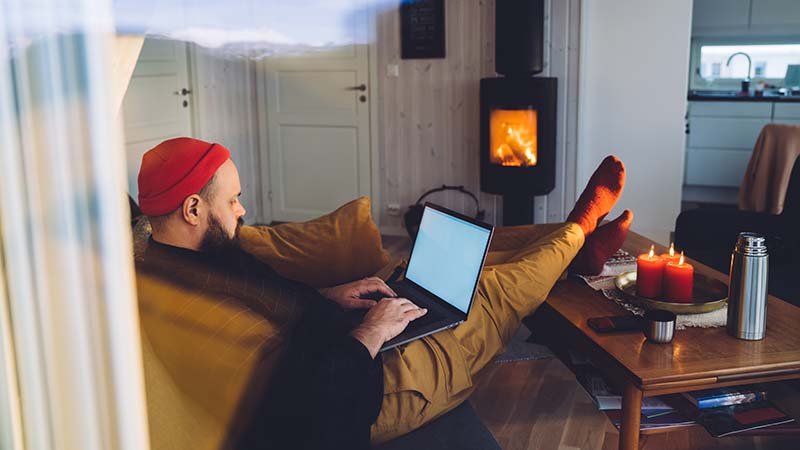 En mann sitter foran peisen med lap toppen i fanget.