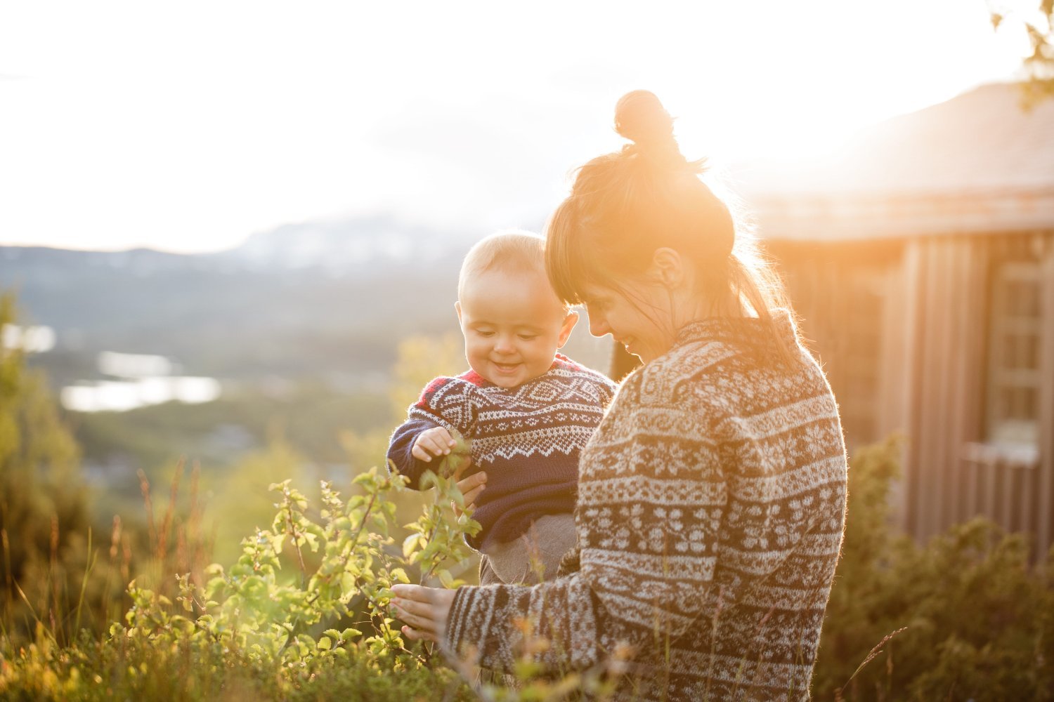 Mor og baby står utenfor et boligbygg og ser på blomster.