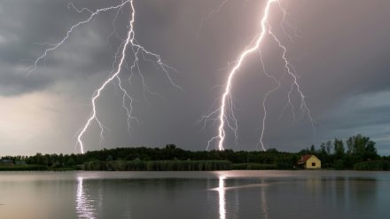 Lyn som slår ned i skogholtet bak en hytte ved vannet.