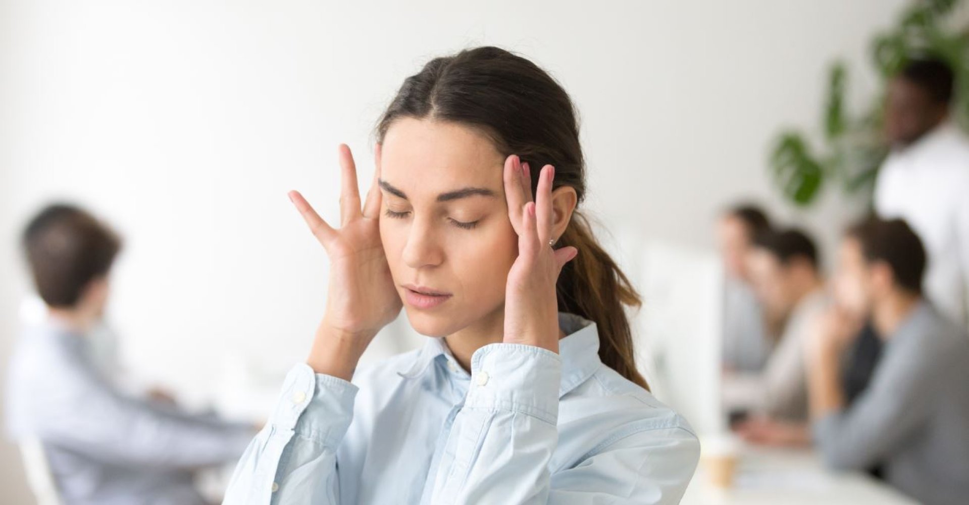 En kvinne legger hendene mot sidene av hodet med lukkede øyne, som om hun kjenner på stress eller anstrengelse.
