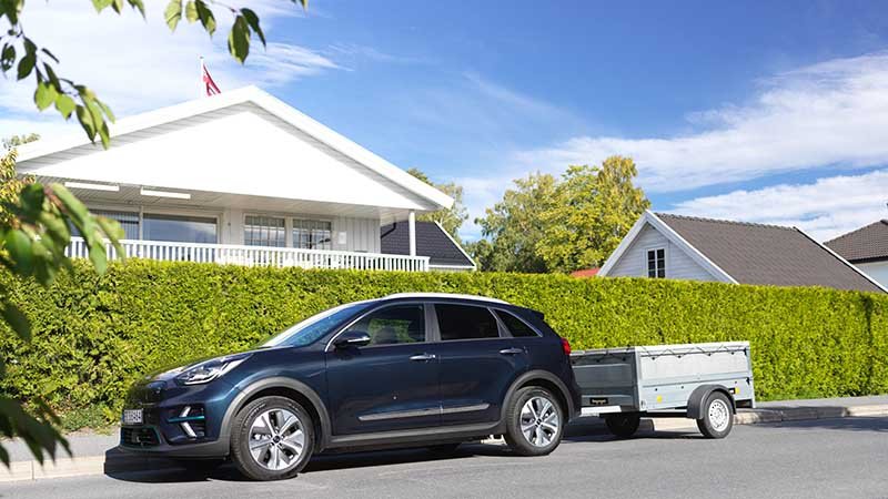 En parkert elbil med tilhenger utenfor et hus.