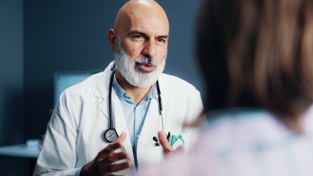 Lege med stetoskop skriver på et blått skjema under en konsultasjon.