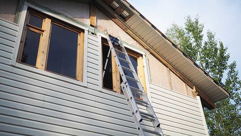Stige lent mot et hus under arbeid med vindusrammer og kledning.